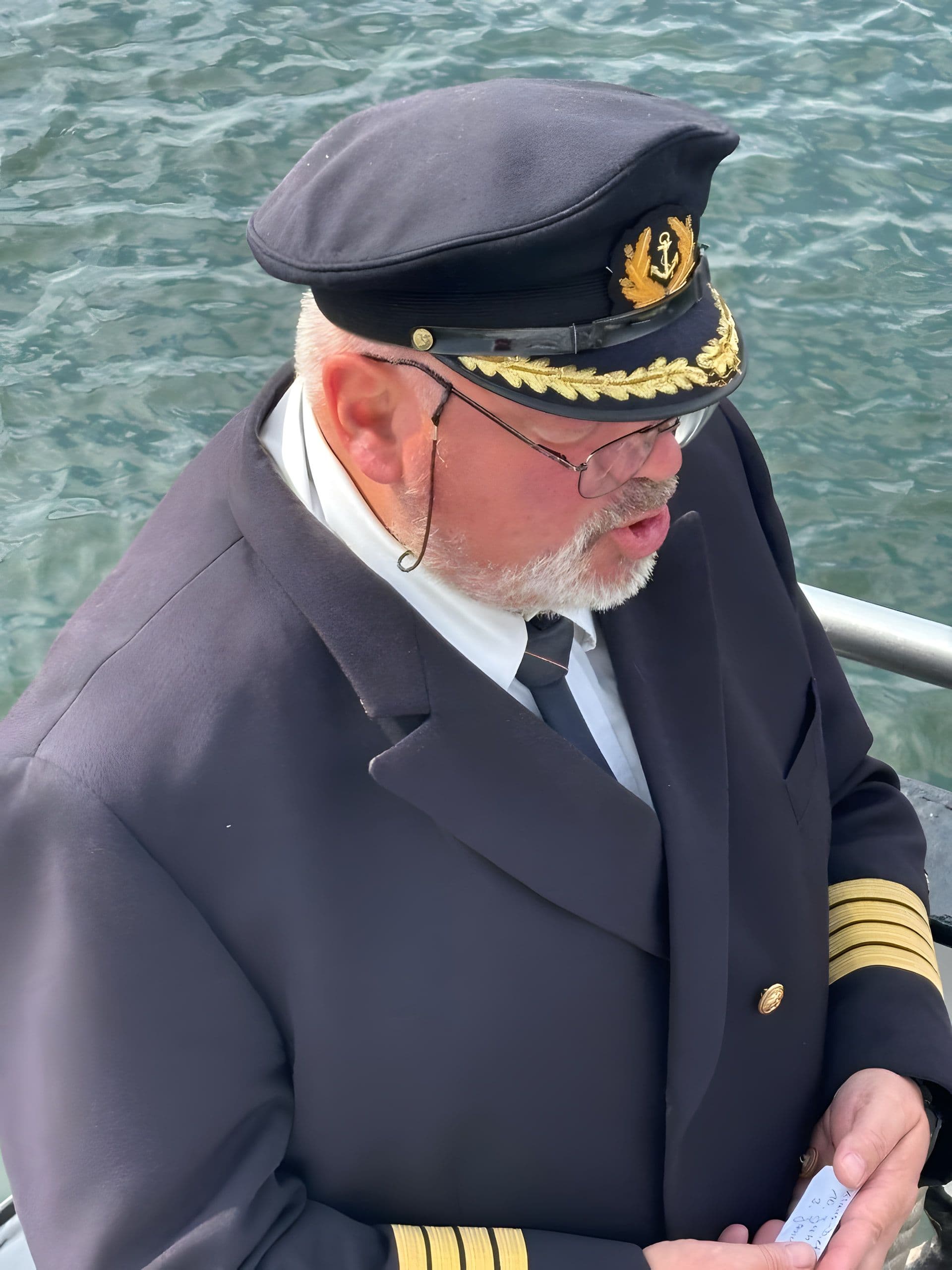 Kapitän in dunkler Uniform mit Ankerstickerei liest Gedenkworte an Bord