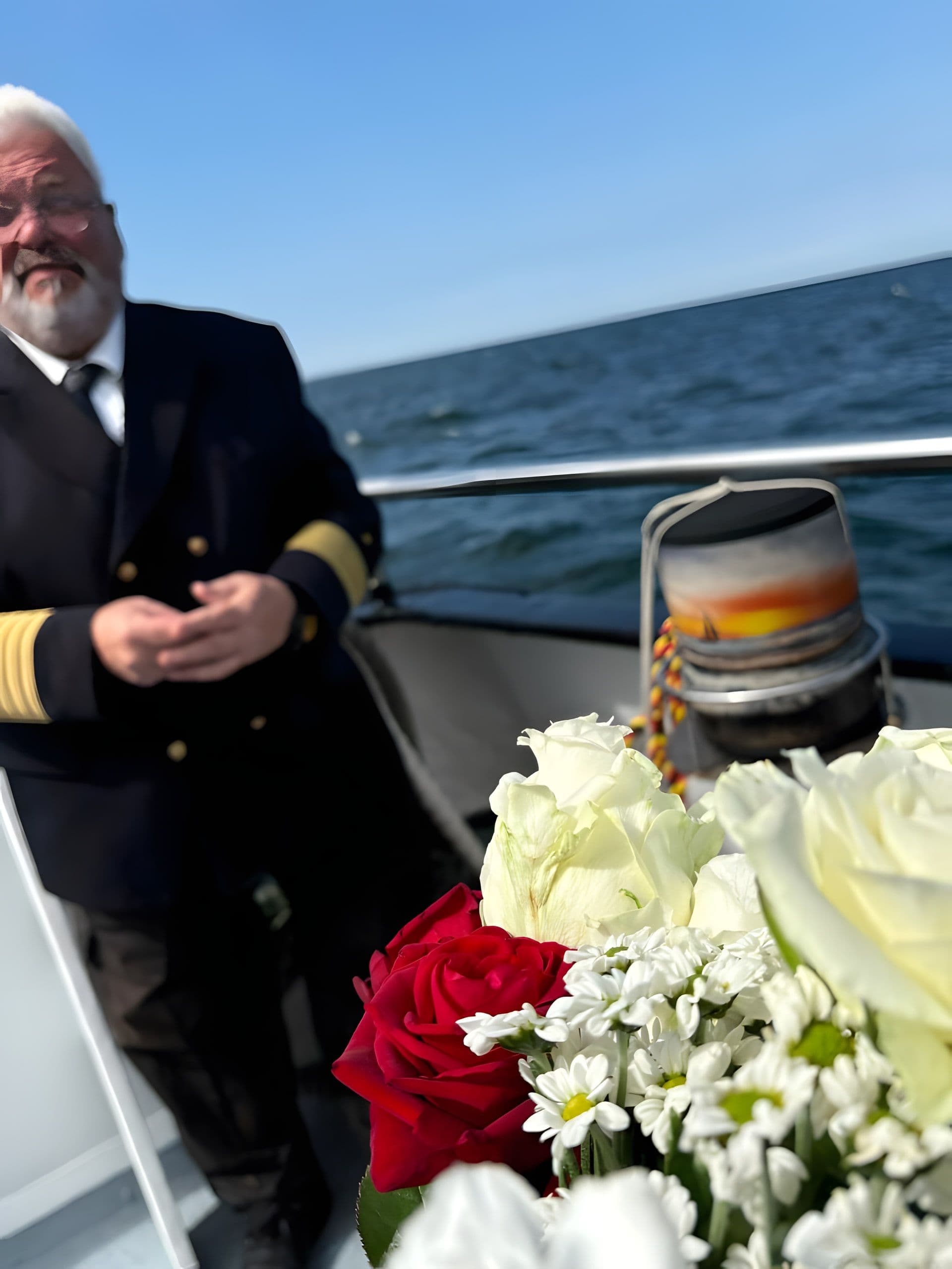 Rote und weiße Rosen an Bord, im Hintergrund der Kapitän auf sonniger Ostsee
