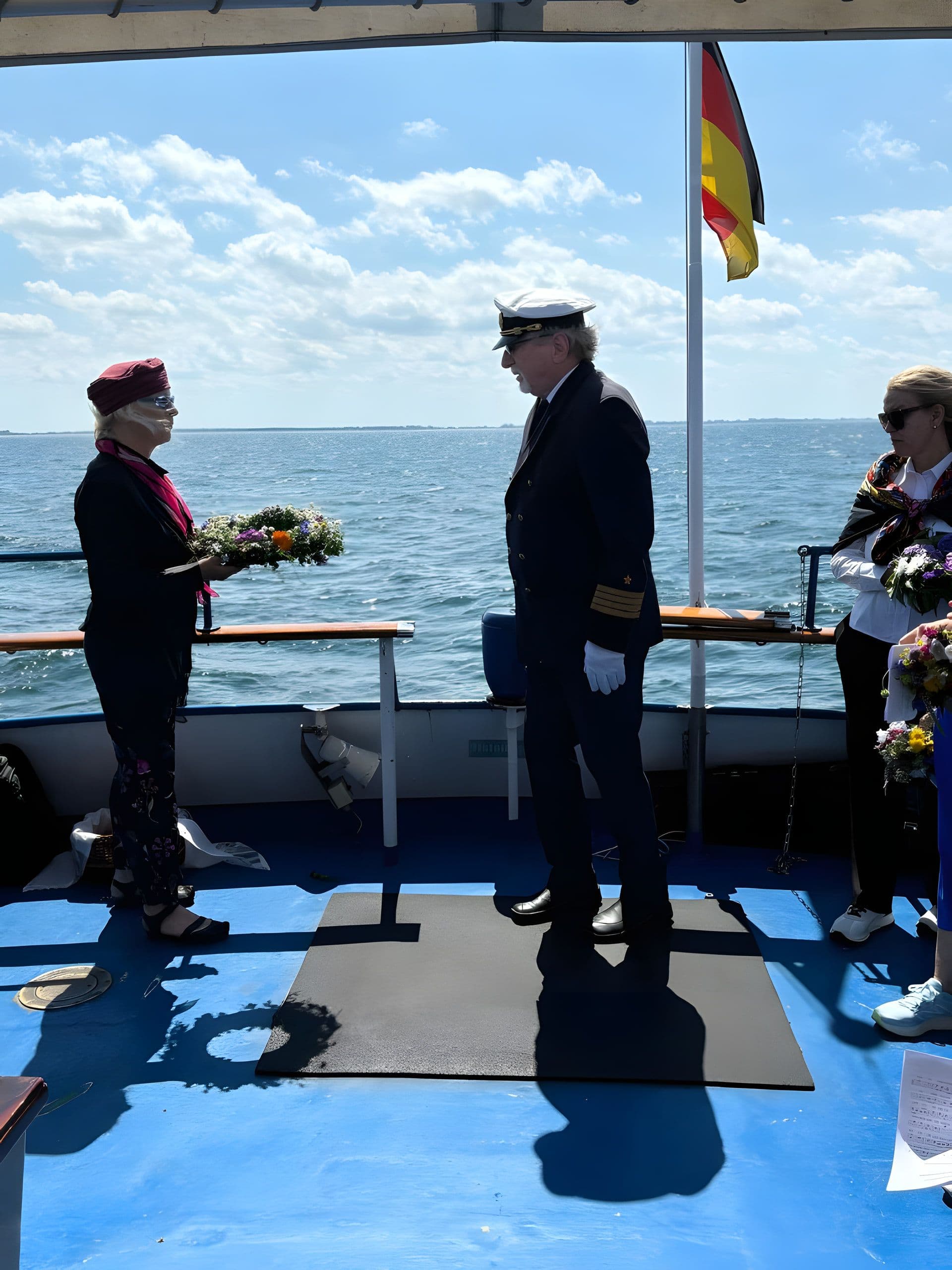 Trauerfeier an Deck: Kapitän in Galauniform, Angehörige mit Blumen, deutsche Flagge am Heck