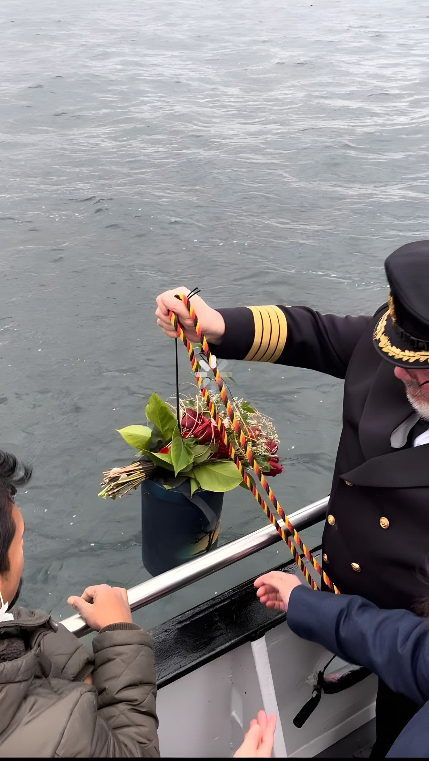 Kapitän übergibt eine mit Blumen geschmückte Seeurne an der Reling dem Meer