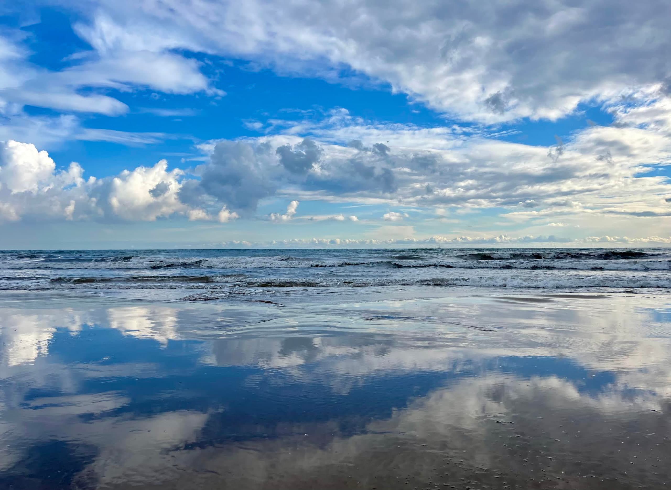 Weite Ostsee bei wechselndem Himmel, Wolken spiegeln sich im nassen Strand