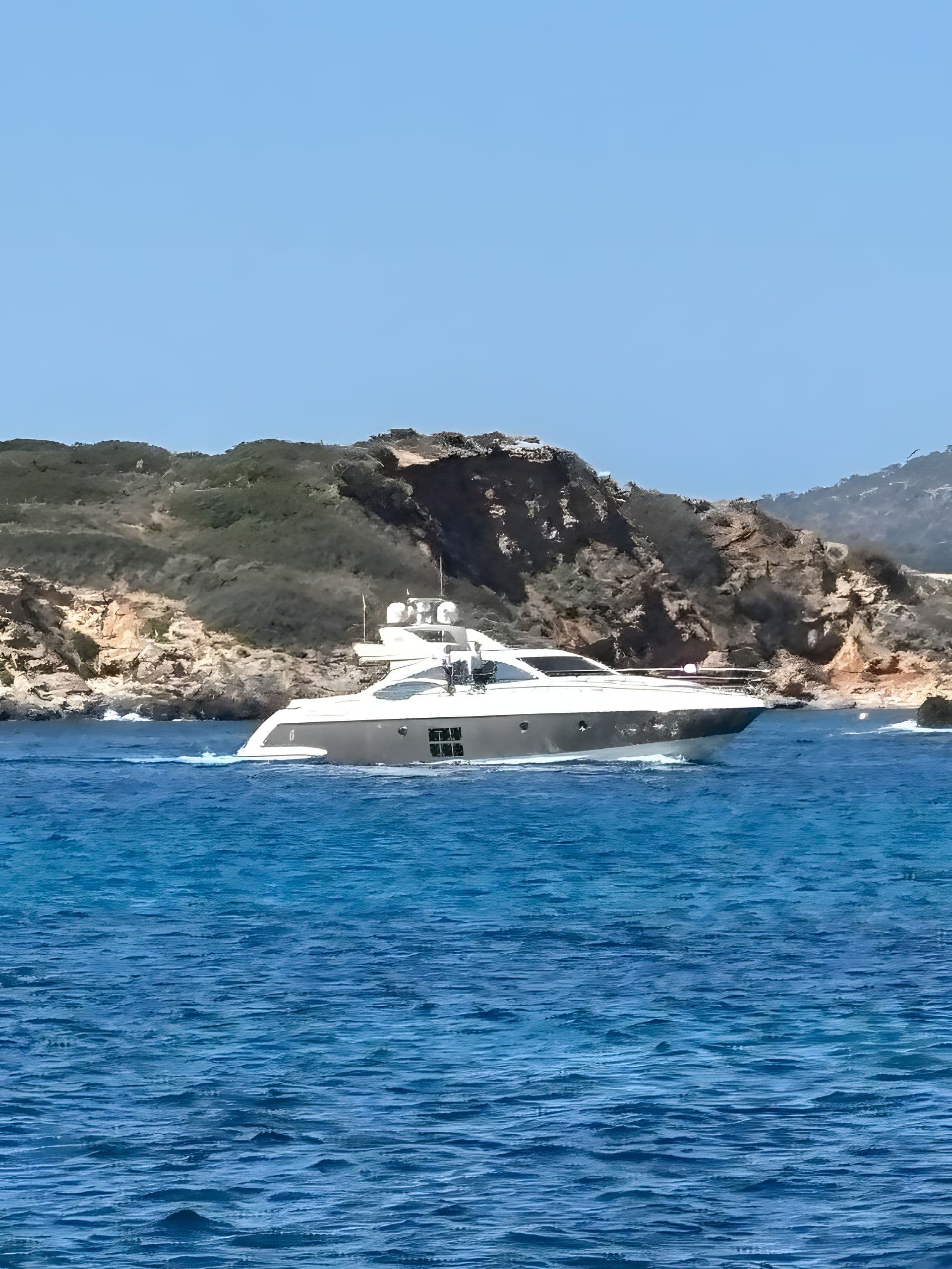 Motoryacht vor felsiger Mittelmeerküste, klares blaues Wasser