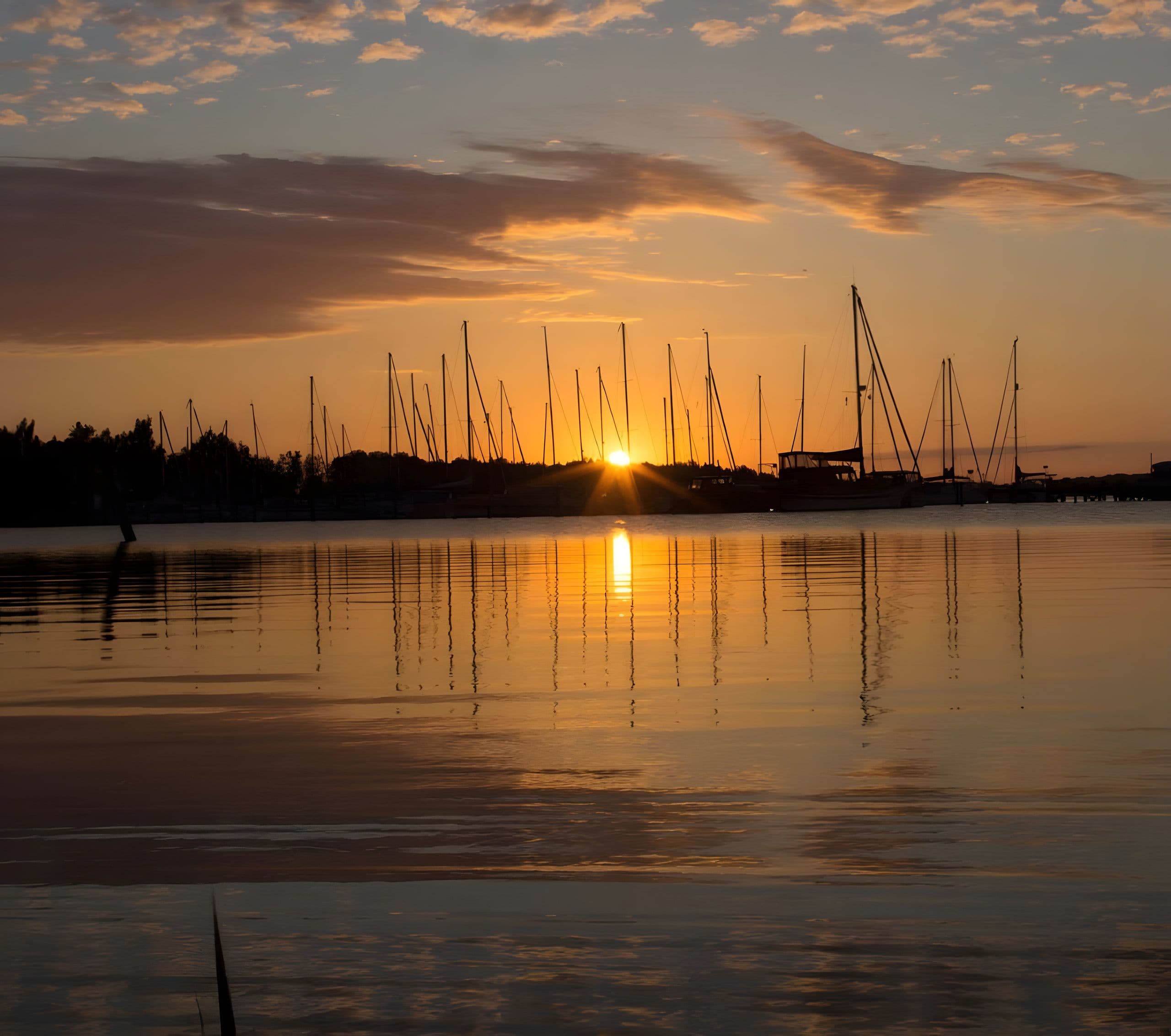 Sonnenuntergang über einem stillen Hafen, Masten spiegeln sich im Wasser